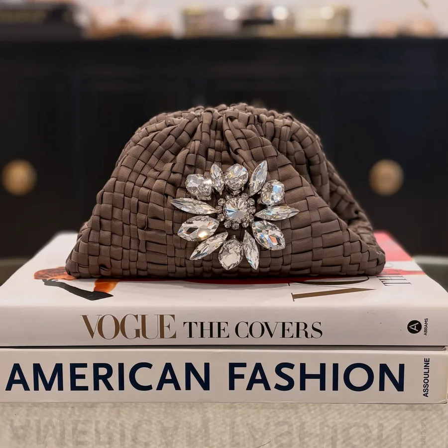 A woven clutch with a crystal brooch on a stack of Vogue books