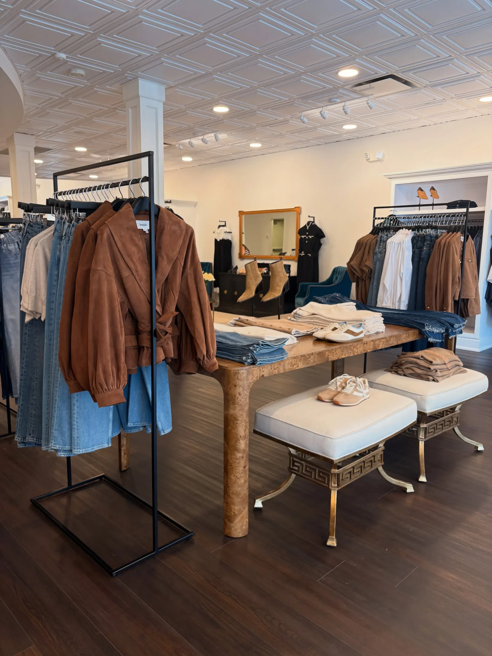 The women’s floor at the front of the store: a burl-wood table and cream benches between racks of jackets and denim