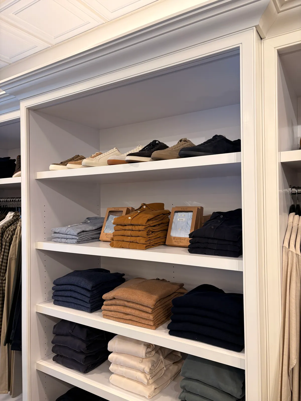 Built-in shelves of folded sweaters in navy, camel and cream, with shoes on the top shelf