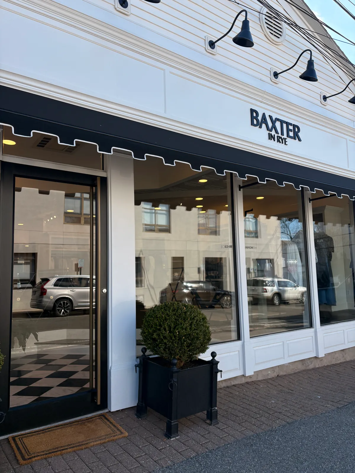 The side entrance under the black scalloped awning, a boxwood by the glass door and marble floor