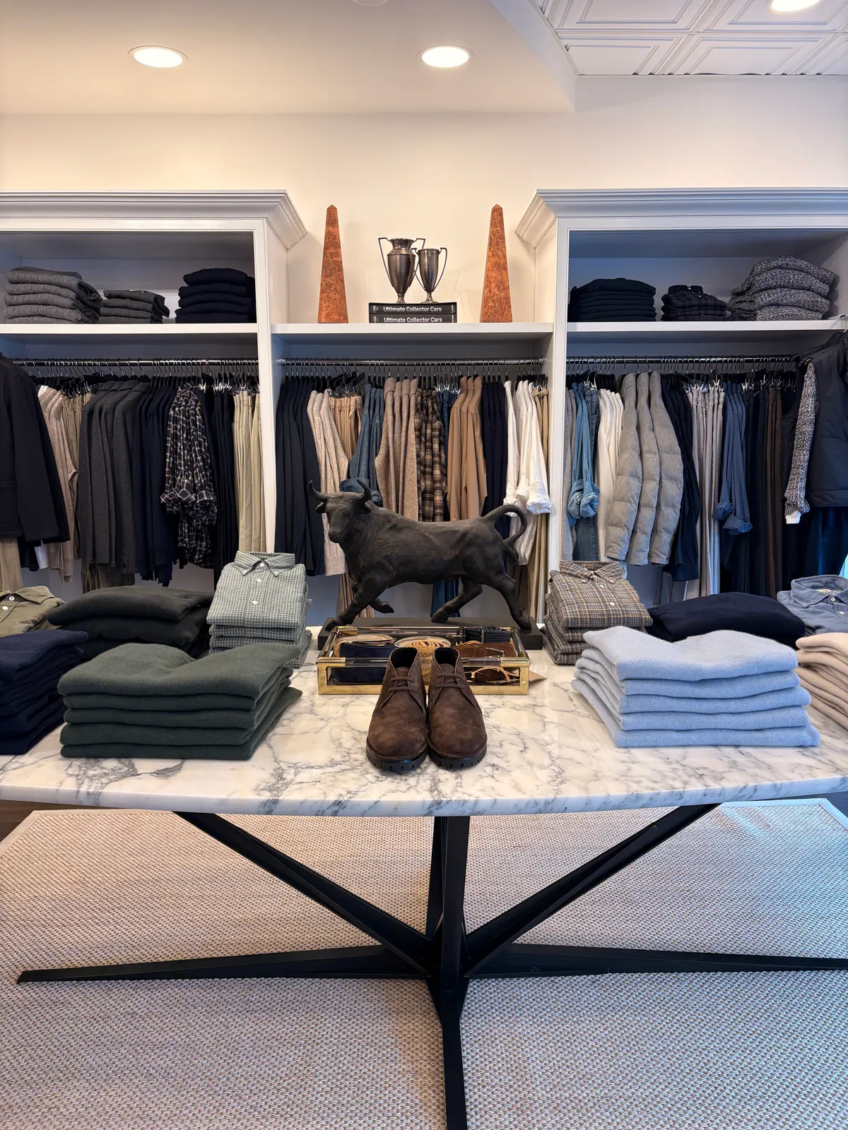 A marble table with a bronze bull, folded knits and suede shoes, shelves of menswear behind
