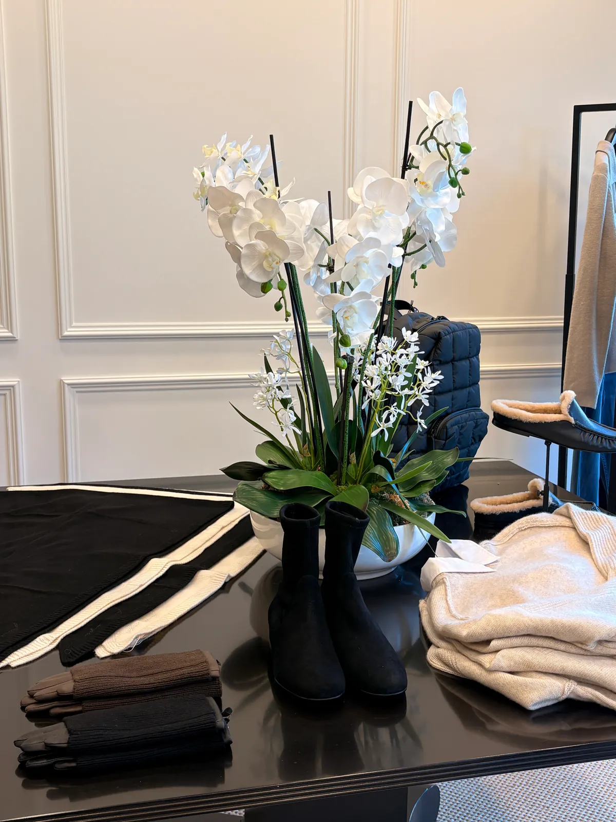 White orchids on a black table with folded knits, boots and gloves