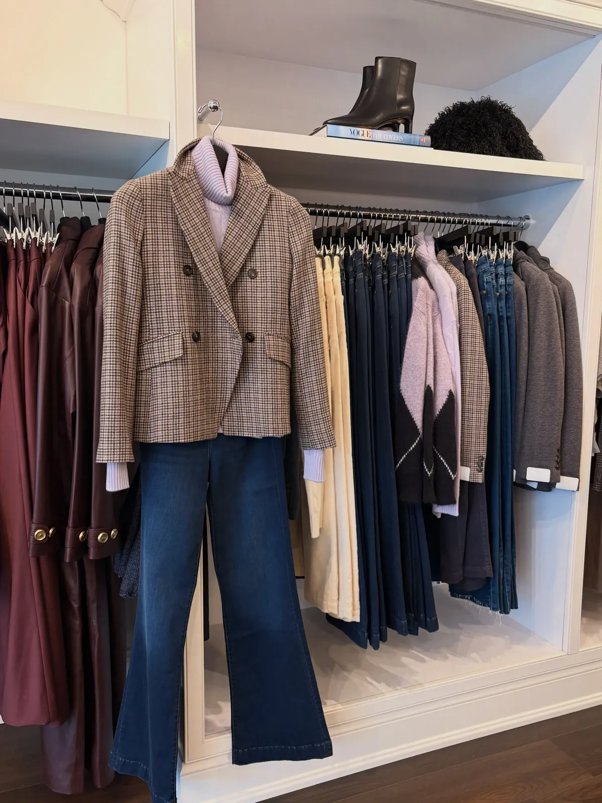 A look pulled together on a hook: a plaid double-breasted blazer over a lilac shirt and flared jeans, with boots on the shelf above