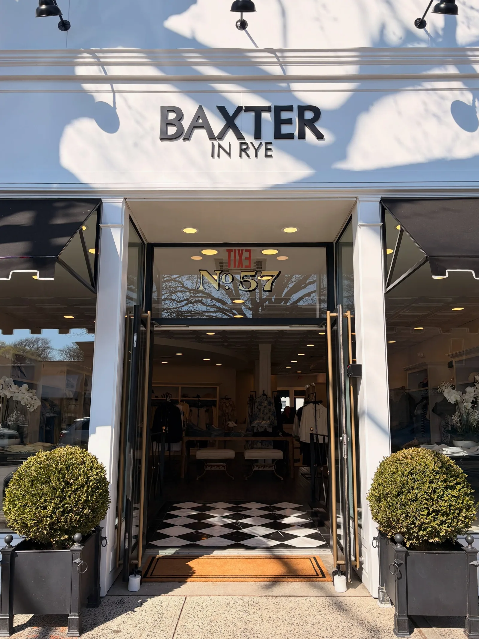 The Baxter in Rye storefront on Purchase Street, doors open onto a black-and-white marble entry, boxwoods on either side